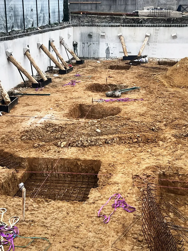 Paroi de fouille blanche maintenue par une rangée de rondins inclinés, fond de fouille en terre.