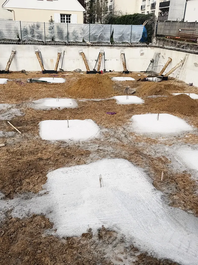 Fond de fouille avec semelles en béton coulées, attentes en acier dressées.