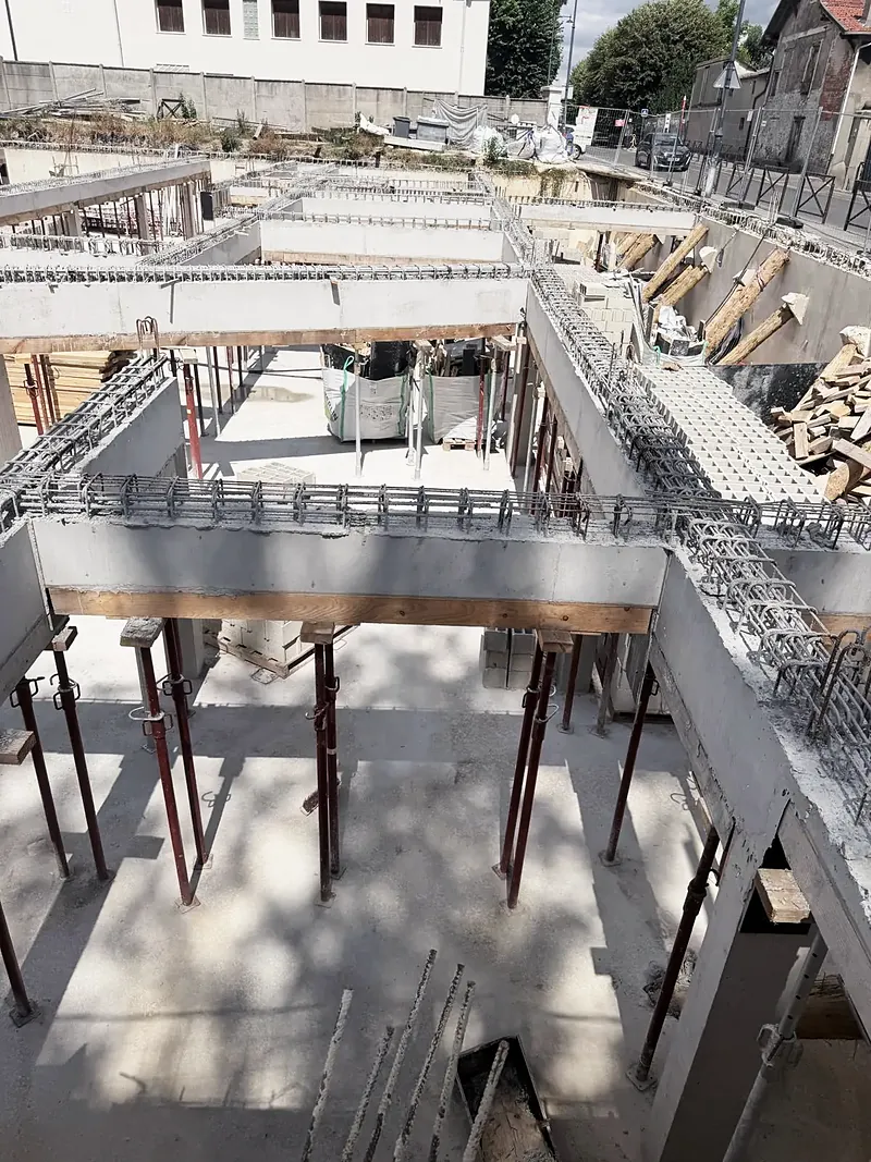 Poutres en béton coffrées en bois et étayées par des étais métalliques rouges au-dessus de murs en blocs.