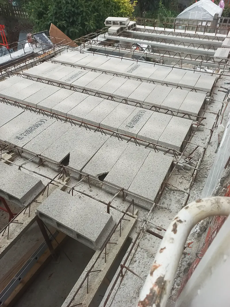 Plancher en cours de pose, entrevous béton gris entre des poutrelles, armatures de chaînage et chapeaux en acier.