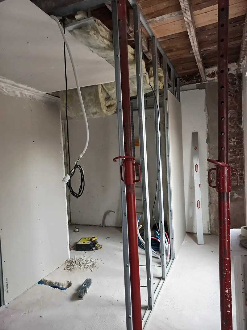 Pièce en travaux, étais rouges sous un plafond en planches et solives bois, cloison en plaques de plâtre sur ossature métallique.