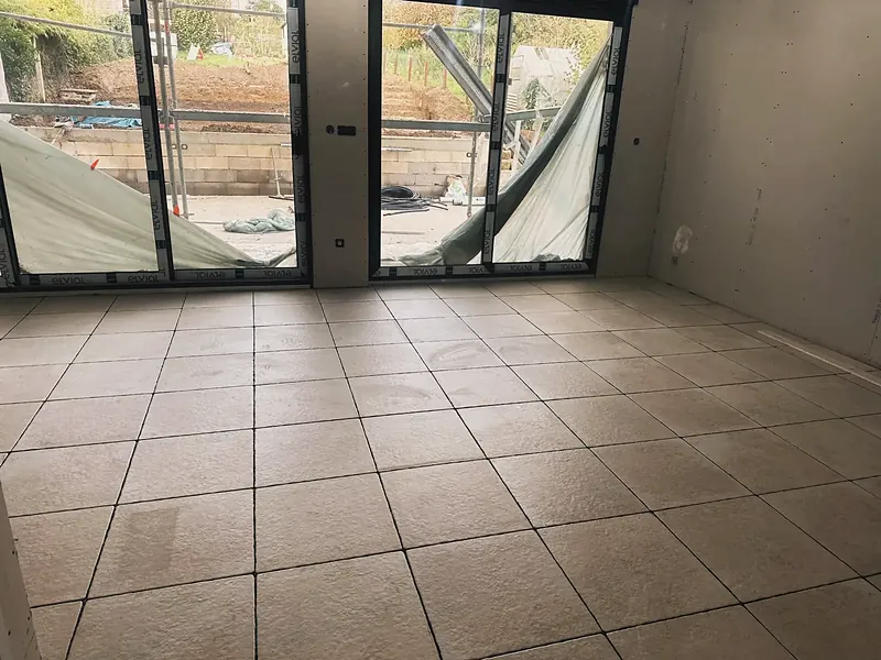 Pièce de vie avec carrelage beige grand format et deux baies vitrées coulissantes.