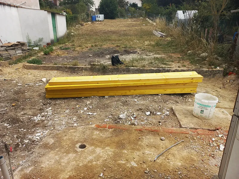 Jardin en longueur, terre à nu, madriers au premier plan.