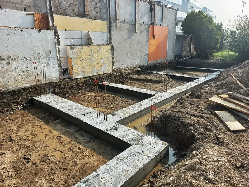 Semelles de fondation en béton coulées en forme de L, fers d’attente verticaux, fouilles humides autour.