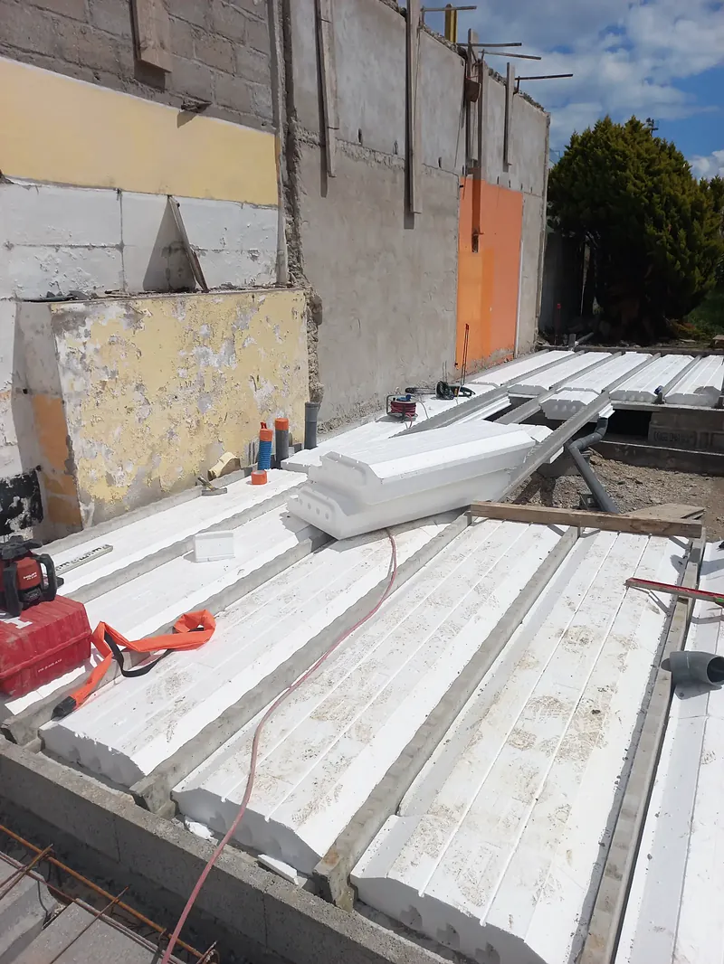 Plancher en cours de pose : entrevous blancs en polystyrène entre des poutrelles béton, sur un soubassement en blocs.