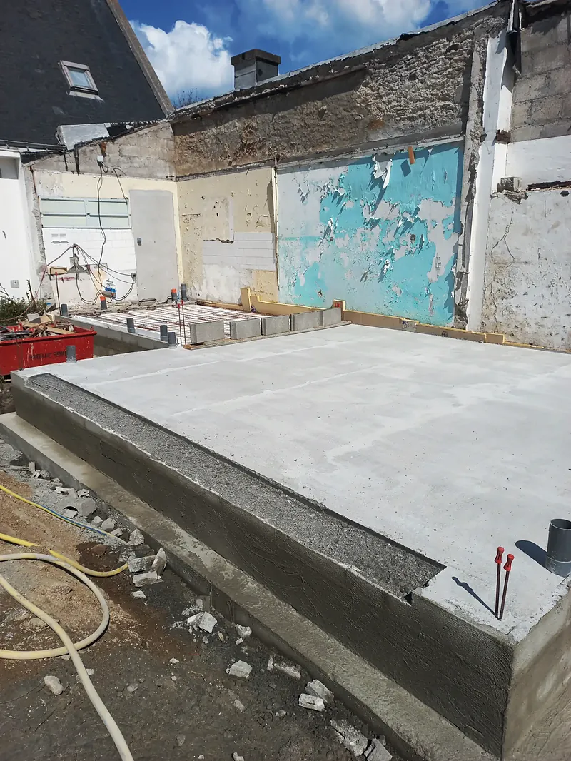 Dalle de béton lisse et fraîchement coulée sur son soubassement, tuyaux de réseaux en attente.