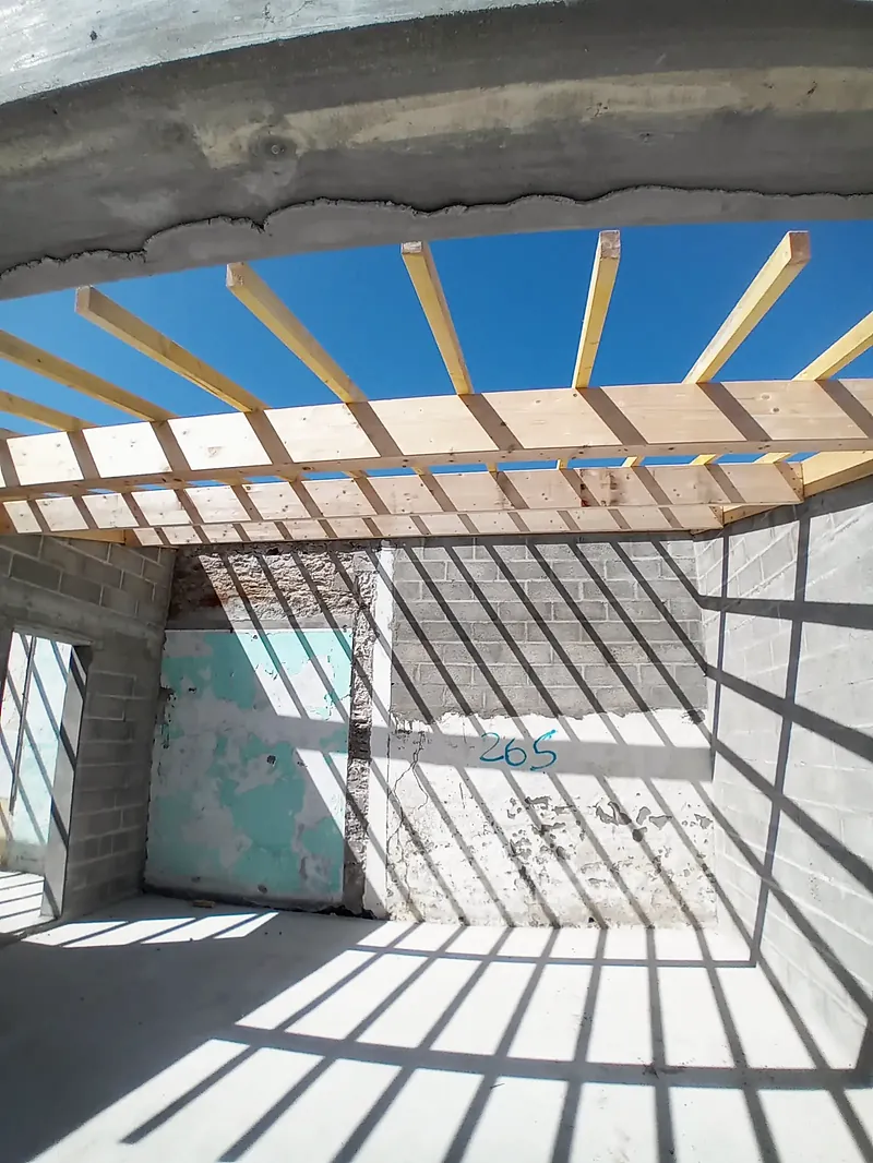Vue vers le ciel à travers un solivage en bois clair posé sur des murs en blocs béton.