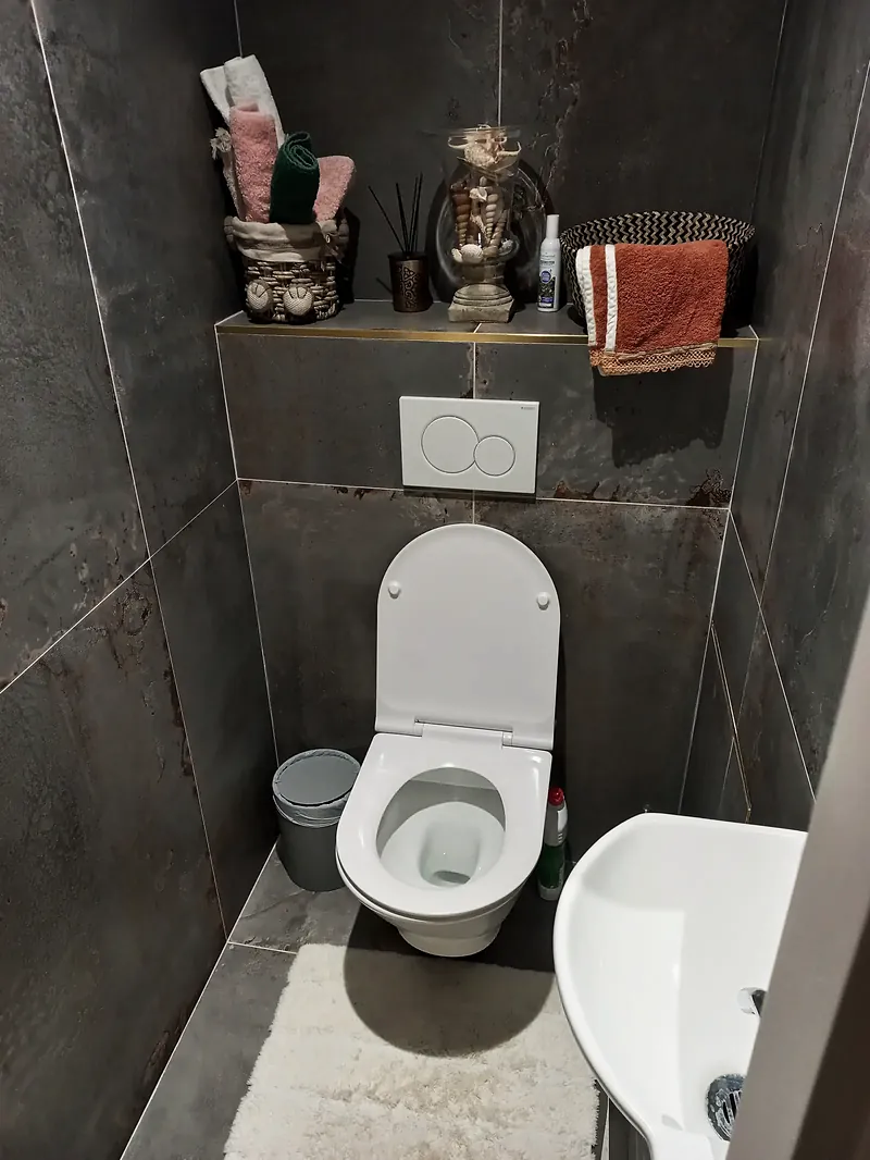 WC suspendu blanc et lave-mains devant un carrelage grand format gris-rouille, tablette carrelée à profilé doré.