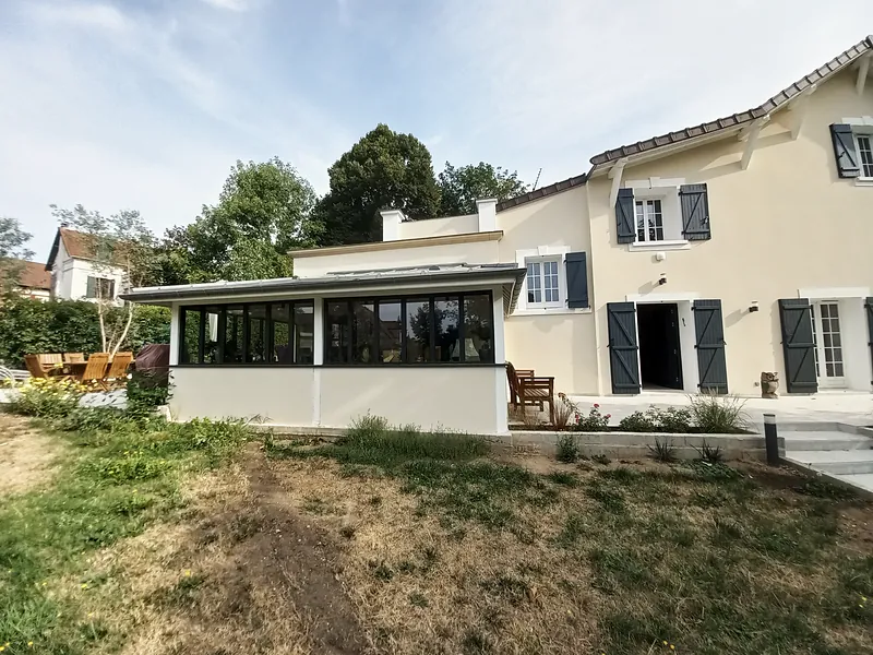 La maison et sa pièce vitrée, couverture métallique et volets gris.