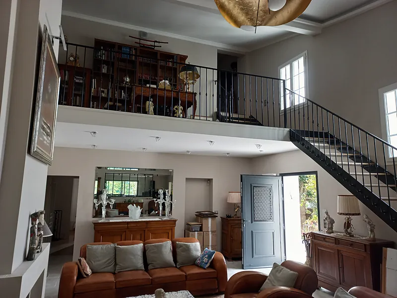 Le séjour sous la mezzanine : bibliothèque en galerie, escalier métallique noir.