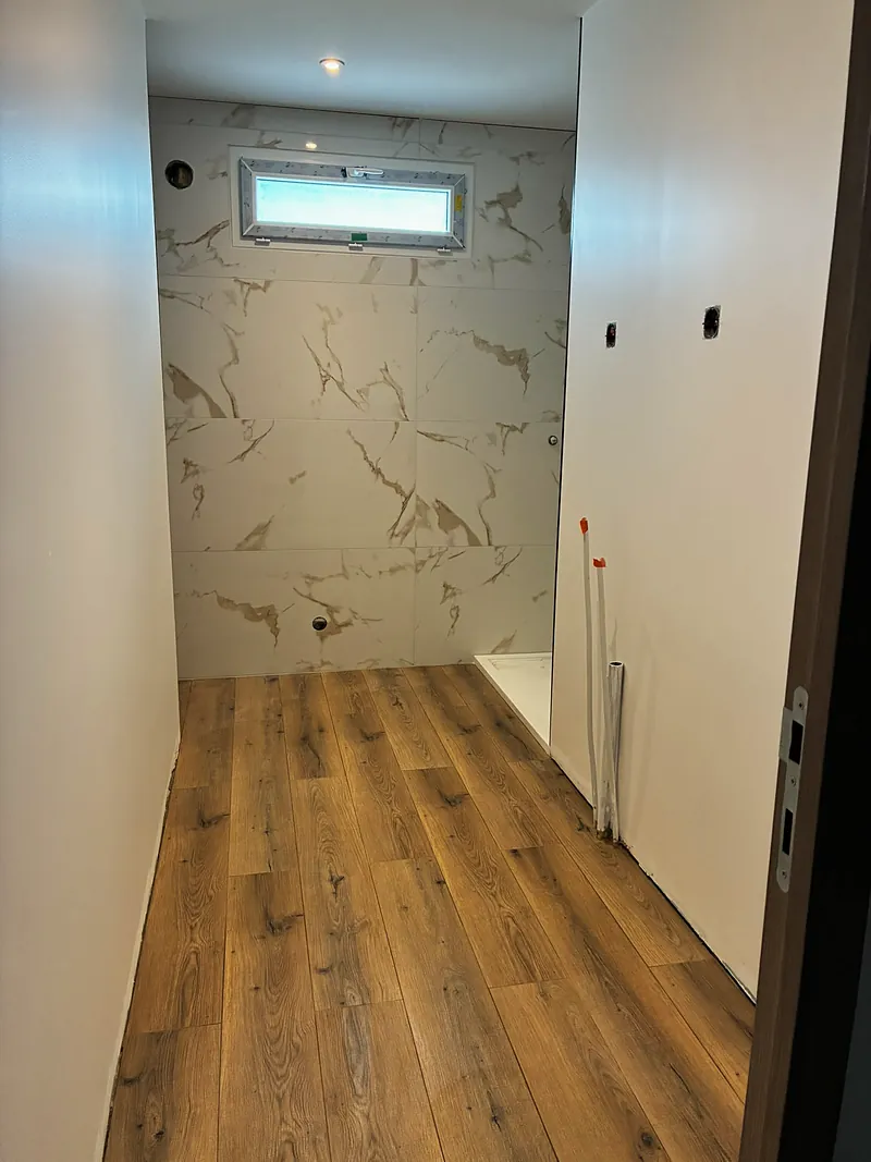 Pièce d’eau en cours : mur en carrelage effet marbre, sol en bois.