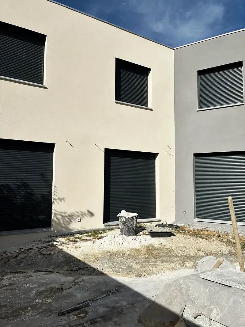 Angle de façades enduites claires avec fenêtres anthracite à volets roulants.