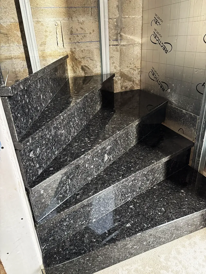 Marches d’escalier habillées de pierre noire mouchetée polie.