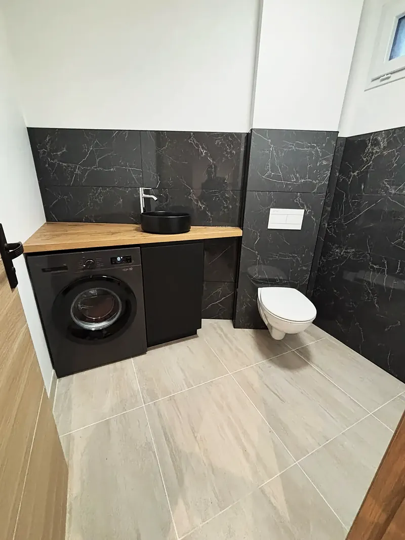Pièce d’eau avec faïence effet marbre noir, plan vasque en bois, vasque noire et WC suspendu.
