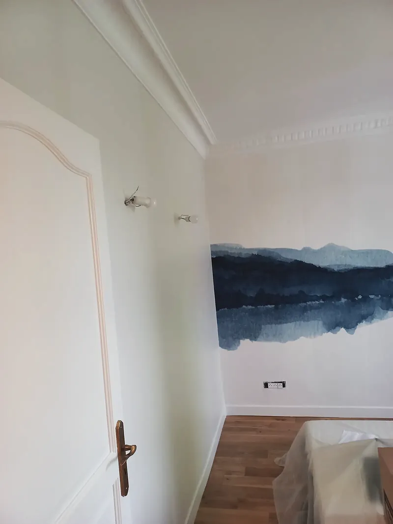 Chambre aux murs blancs avec papier peint panoramique de montagnes bleues, corniche moulurée, porte à moulure cintrée, parquet clair.