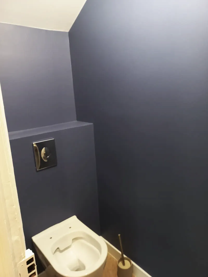 WC suspendu blanc devant des murs peints en bleu ardoise, plaque de commande métallique sur un coffrage.