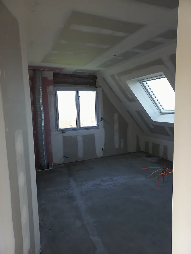 Chambre mansardée aux plaques jointoyées, fenêtre de toit dans le rampant, fenêtre dans le pignon, sol brut.