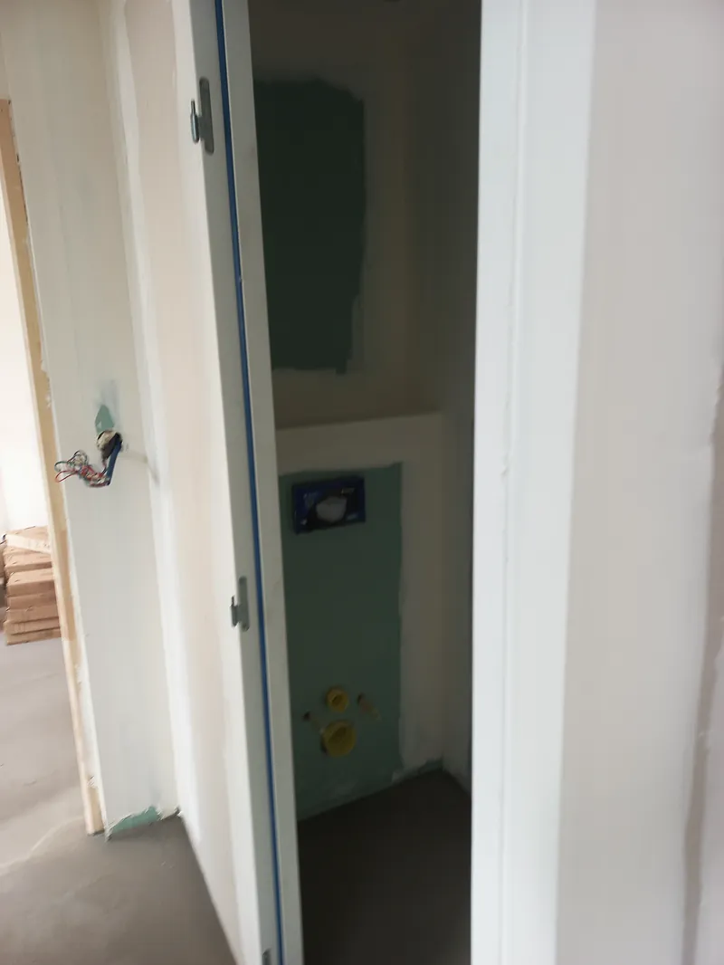Bâti-support de WC suspendu dans un coffrage en plaques de plâtre vertes, porte ouverte au premier plan.