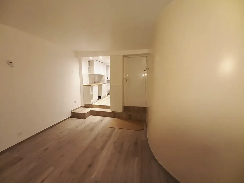 Couloir avec mur courbe blanc menant à l’estrade de la cuisine, spots au plafond.