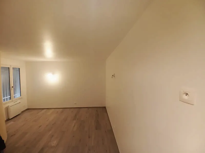 Pièce vide avec sol stratifié clair, appliques murales, fenêtre et radiateur.
