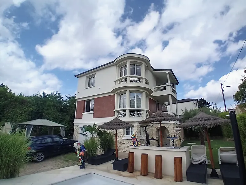Façade sur jardin de la villa surélevée, piscine au premier plan, ciel nuageux.